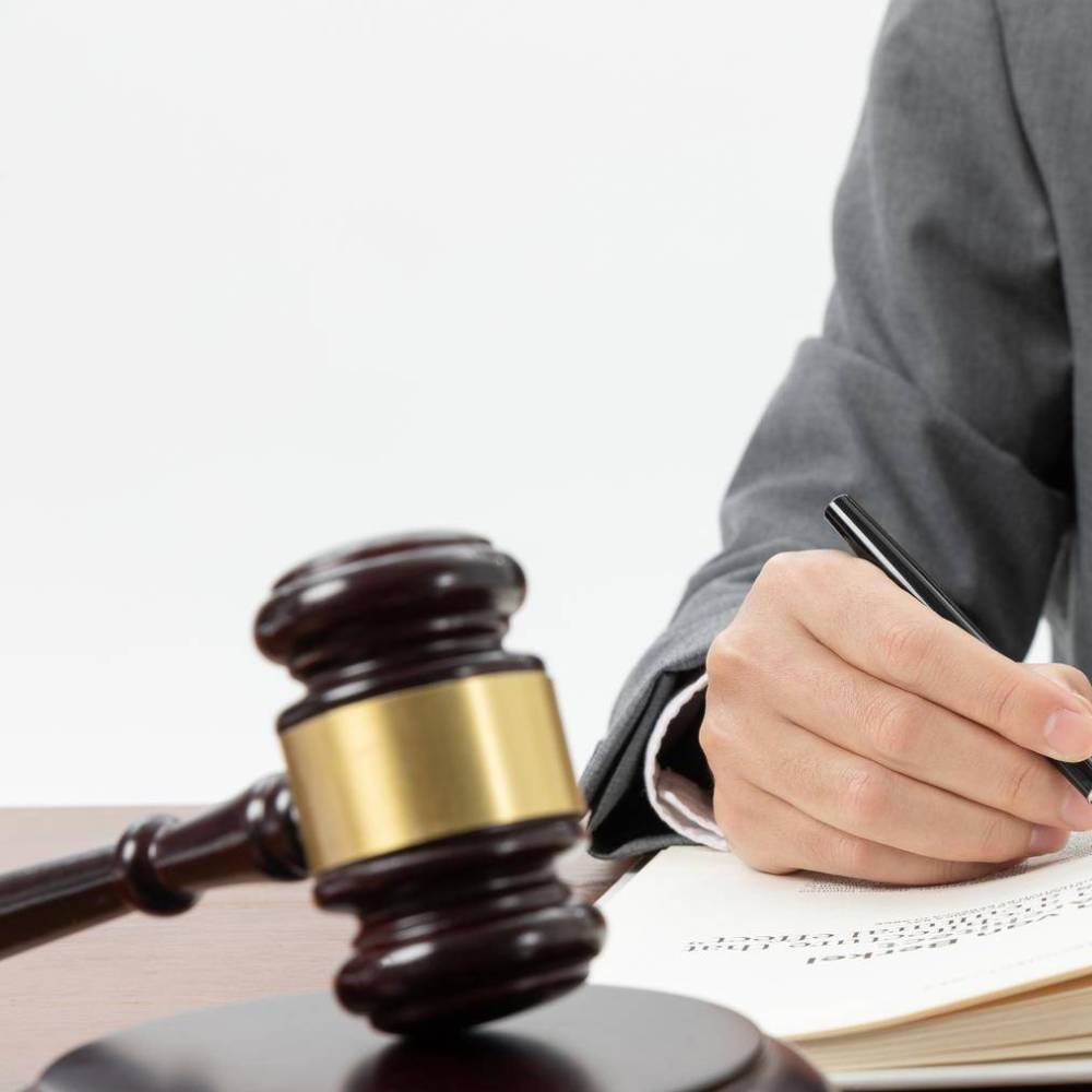 A gavel on a desk in front of someone in a suit writing in a book.