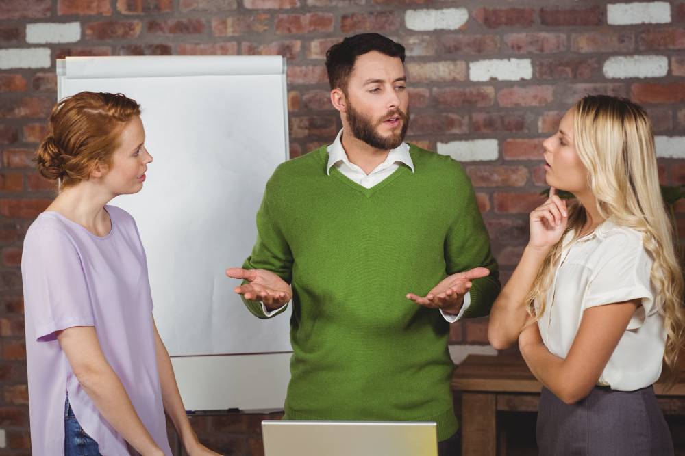 Three paralegals talking together around a laptop in front of a large notepad on an easel.