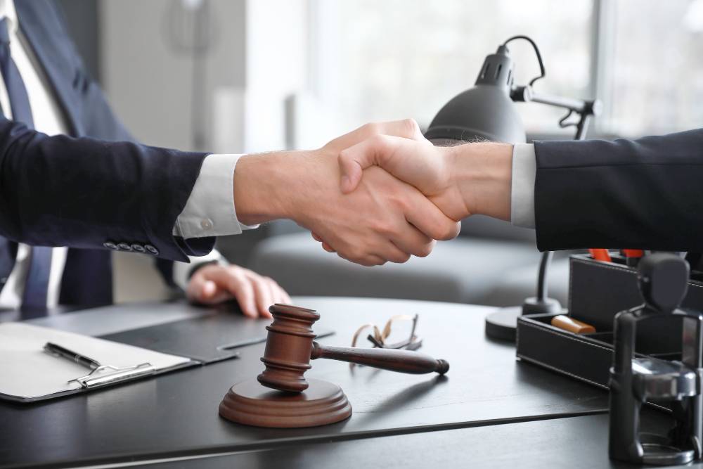 Two people shaking hands over a desk with a gavel on it.