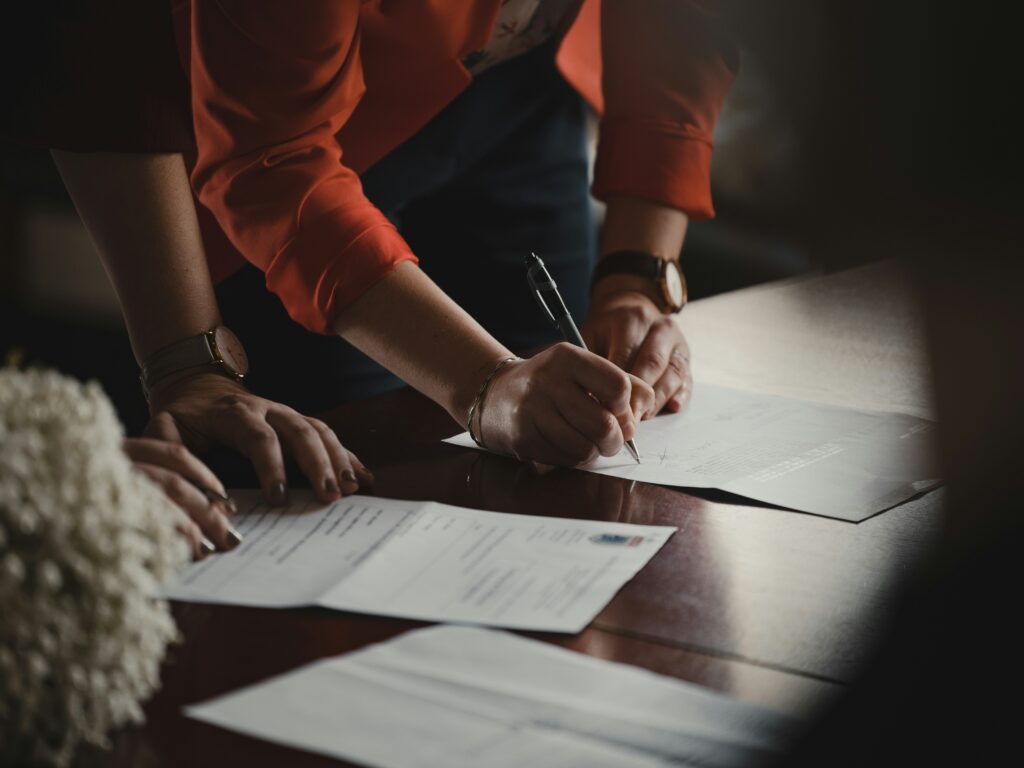 A female lawyer signs documents with a client on a large wooden table.